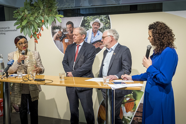 Four people engage in a panel discussion at a podium, with a backdrop featuring agricultural imagery.