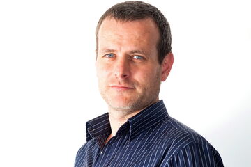 A man in a striped shirt looks confidently at the camera against a plain white background.