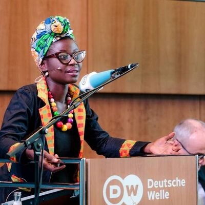 Eine Frau mit farbigem Kopftuch spricht leidenschaftlich bei einer Deutschen Welle Veranstaltung am Rednerpult.