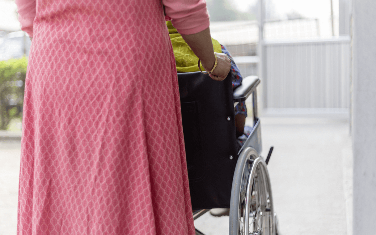 A person in a pink dress is pushing a wheelchair on a clear path, symbolizing inclusive development.