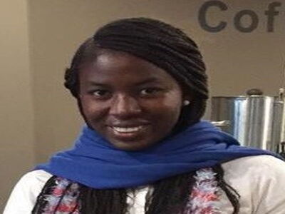 Eine Frau mit blauem Schal lächelt in einem Café in die Kamera.