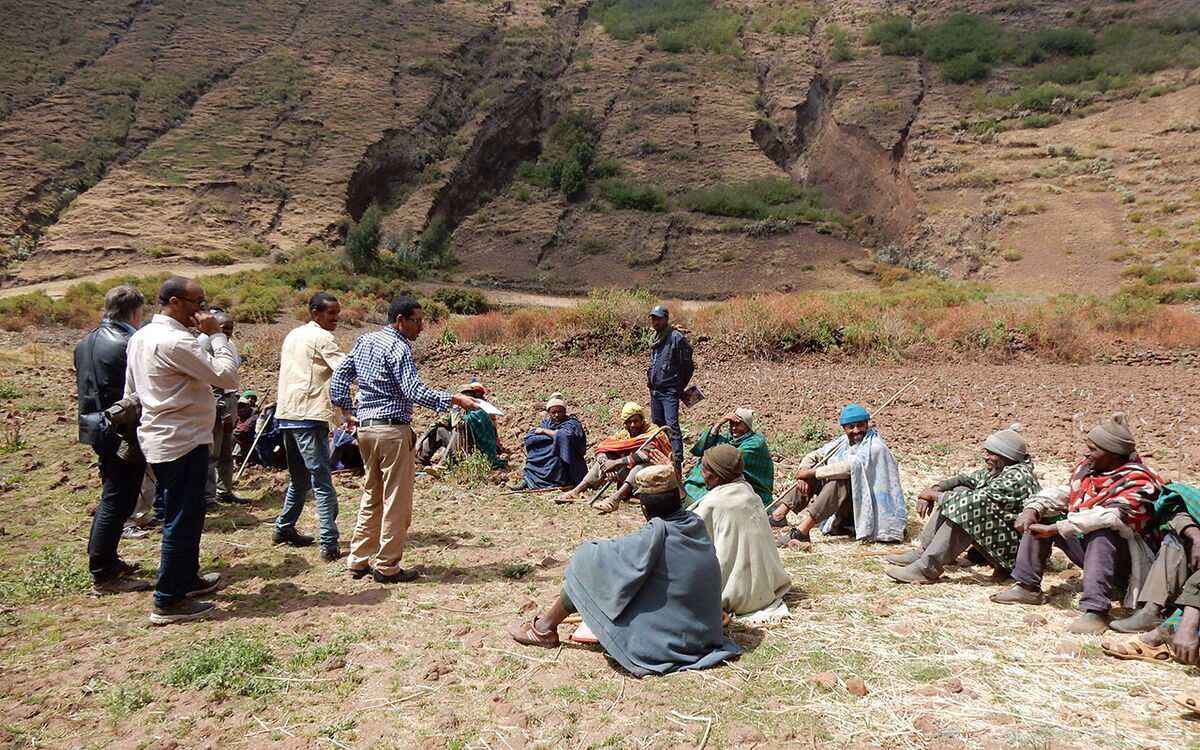 Eine Gruppe von Menschen diskutiert im Freien in einer ländlichen, bergigen Umgebung.