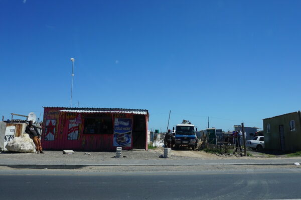 A small roadside shop with colorful signage stands under a clear blue sky next to a parked truck.