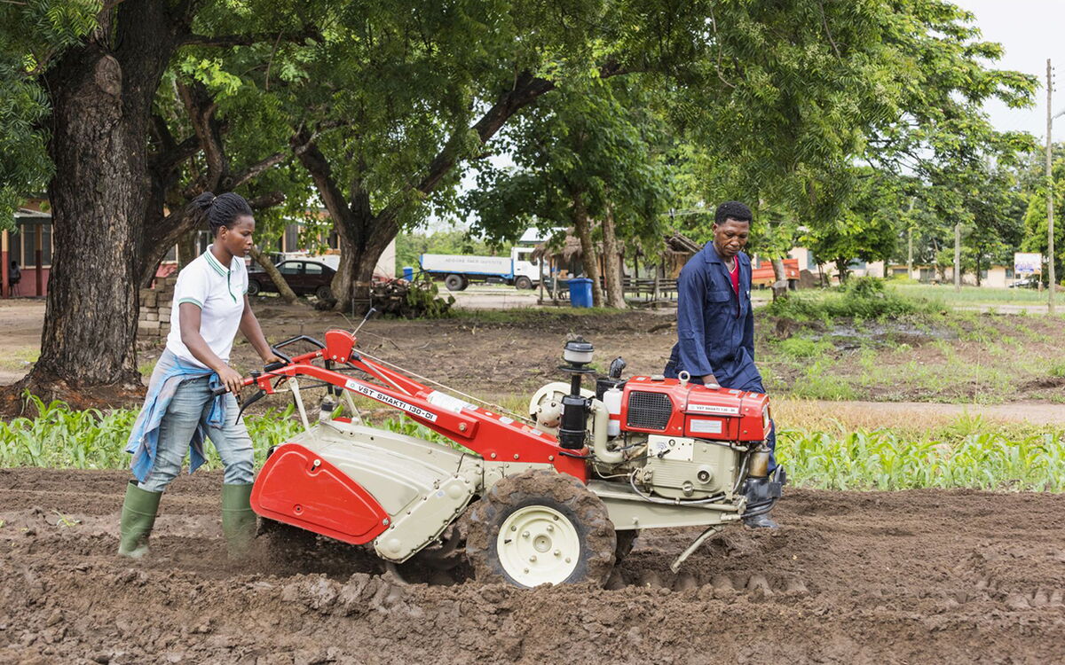Zwei Personen bedienen einen Traktor auf einem Feld, um die Bodenbearbeitung zur Förderung von Dürre-Resilienz durchzuführen.