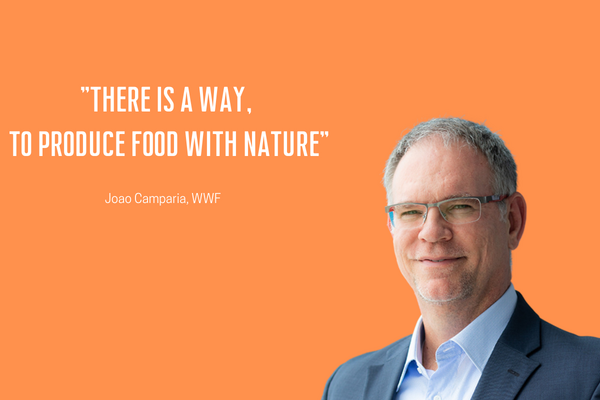 A man in a suit stands against an orange background next to a quote about producing food with nature.