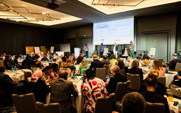 Teilnehmer einer Konferenz diskutieren beim SOILution-P4C-Treffen in einem großen, modernen Konferenzraum.