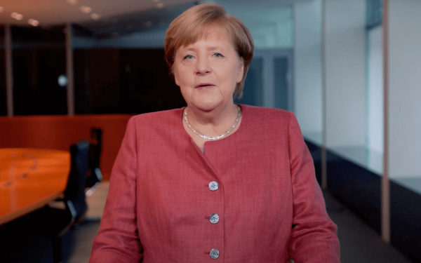 Eine Frau in einem roten Blazer steht in einem modernen Konferenzraum und spricht in die Kamera.