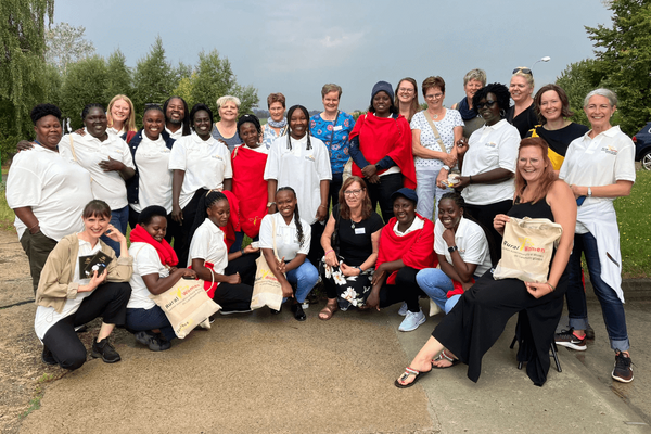 Eine Gruppe von Frauen posiert fröhlich im Freien für ein Gruppenfoto, einige tragen Taschen mit der Aufschrift "Rural Women".