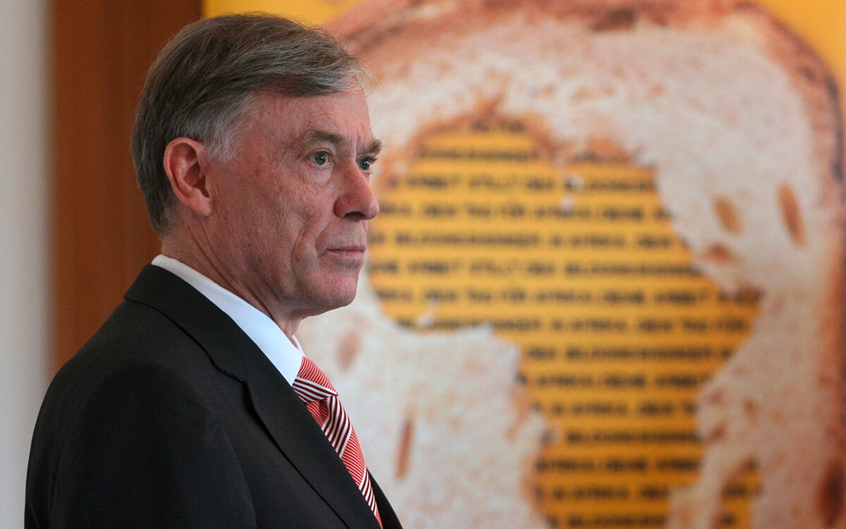 Ein Mann im Anzug steht vor einem Kunstwerk, das eine Brotscheibe mit Text darauf zeigt.