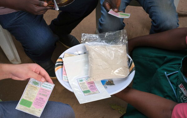 People gather around a bowl holding a package of soy powder, discussing the product information on labels.