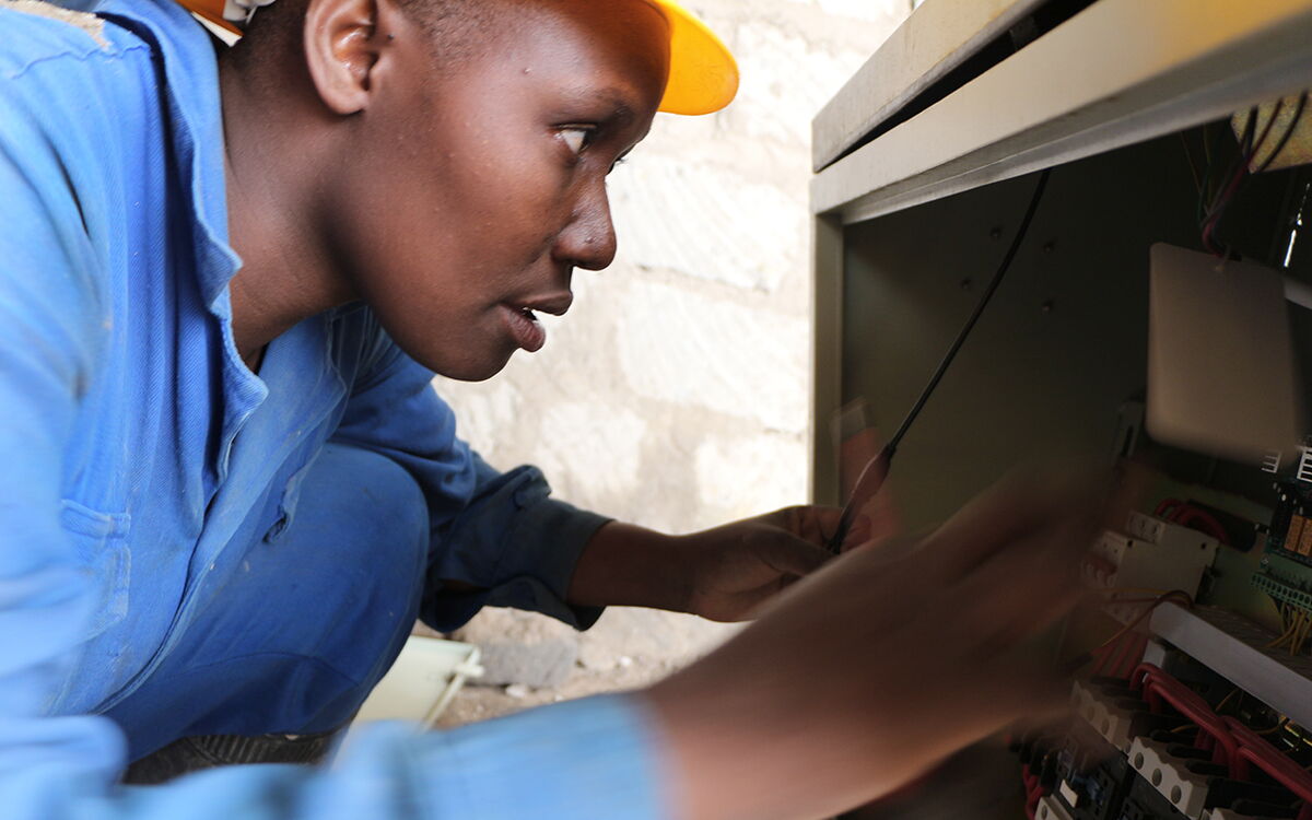 Ein Elektriker in blauer Arbeitskleidung überprüft konzentriert die Verkabelung eines Schaltschrankes.