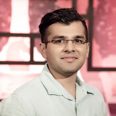 Ein Mann mit Brille und hellem Hemd lächelt vor einem dynamischen, rot beleuchteten Hintergrund in die Kamera.