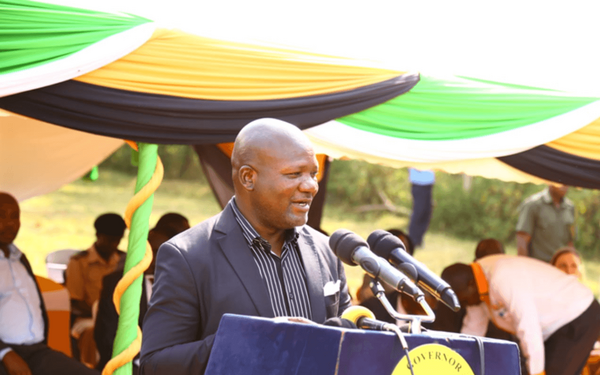 Ein Mann hält eine Rede bei der Farmers Day-Veranstaltung unter einem bunten Pavillon im Freien.