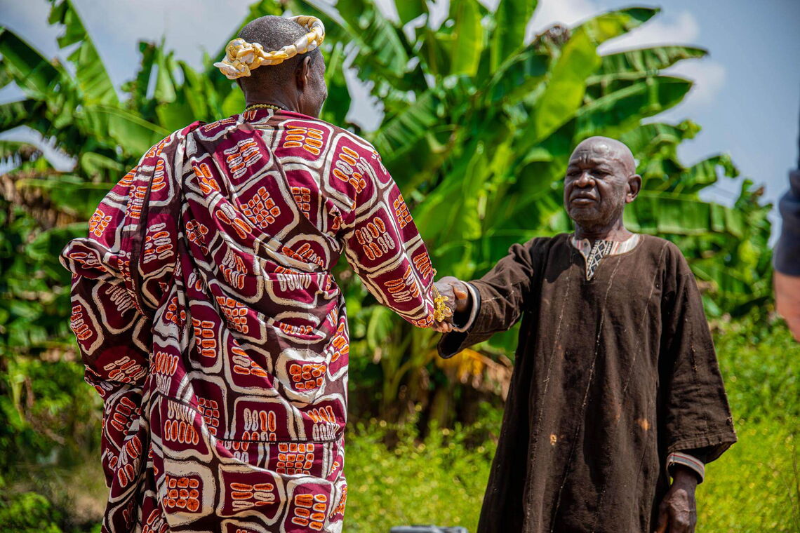 Two chiefs in traditional attire shake hands outdoors, symbolizing an agreement among community leaders.