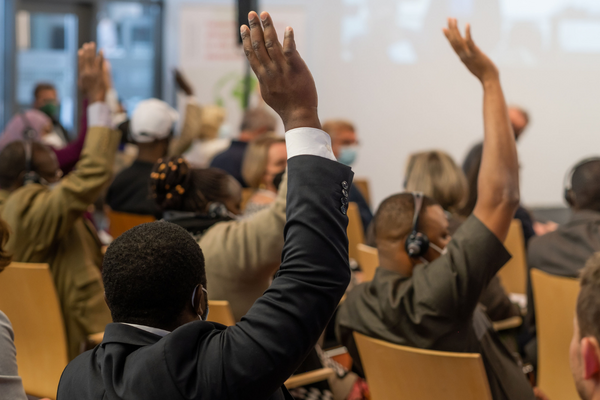 Participants in a conference raise their hands to engage in a discussion on shaping food systems.