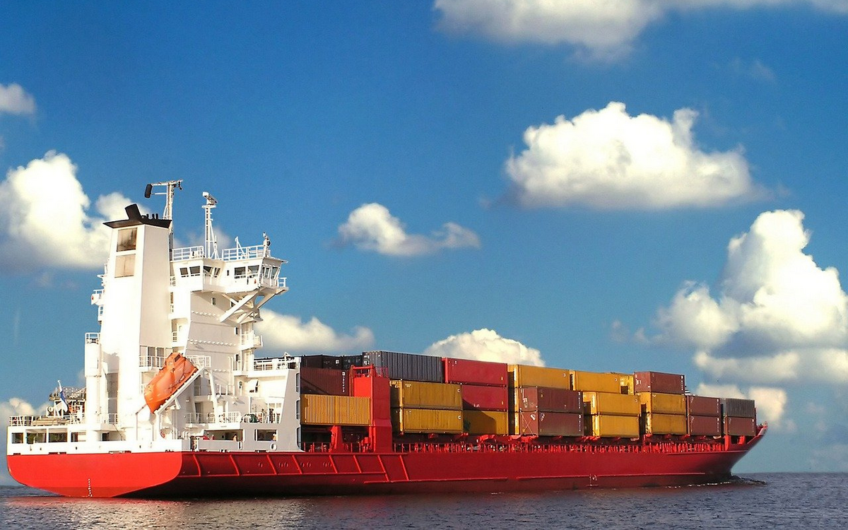 Ein großes Containerschiff mit bunten Frachtboxen fährt unter einem klaren blauen Himmel über das Meer.