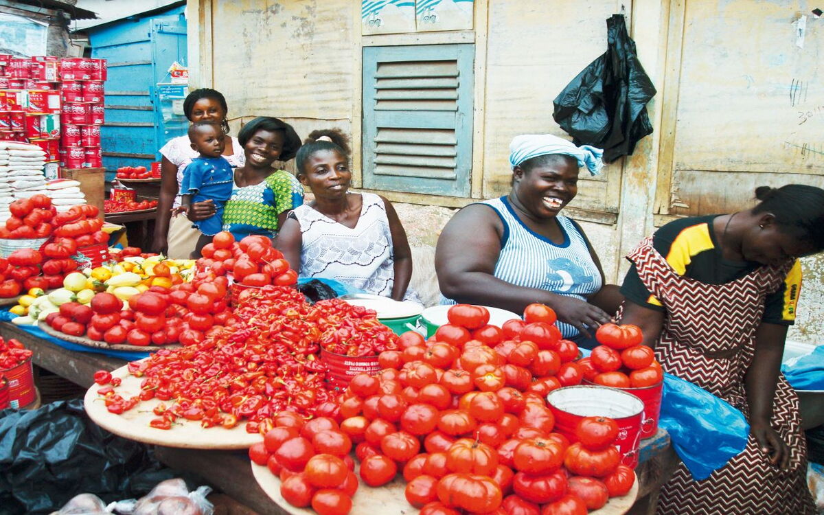 Frauen auf einem Markt in Ghana verkaufen frische Tomaten und Paprika mit einem Lächeln auf den Gesichtern.