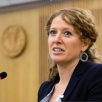 Eine Frau mit lockigem Haar spricht in ein Mikrofon bei einer Konferenz.