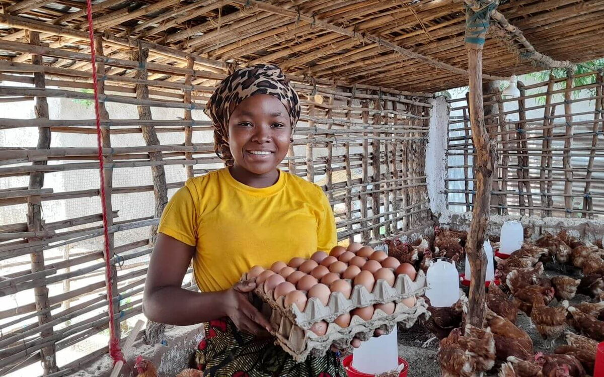 Eine Frau in einem Hühnerstall hält ein Tablett voller Eier und lächelt in die Kamera.