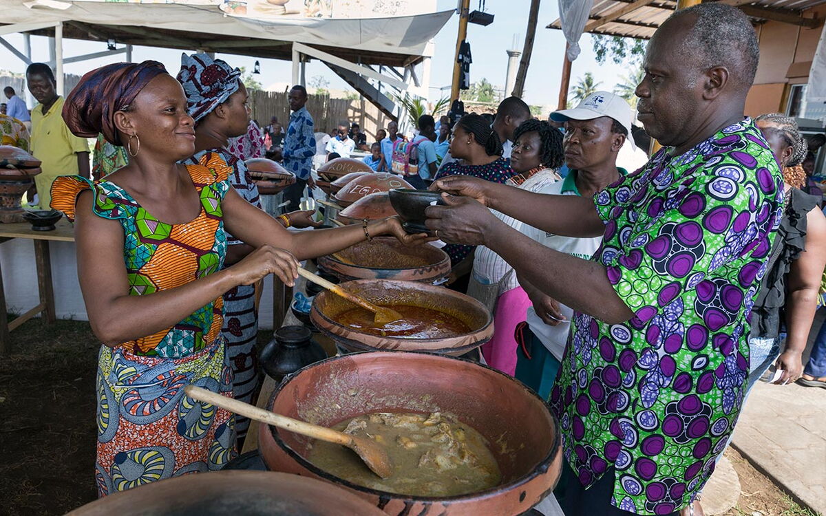 Menschen in bunter Kleidung genießen traditionelle Gerichte auf einem lebhaften Marktstand.