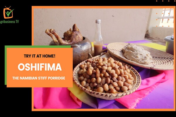 A traditional Namibian meal featuring oshifima, roasted meat, and beans is displayed on woven baskets with a colorful cloth.