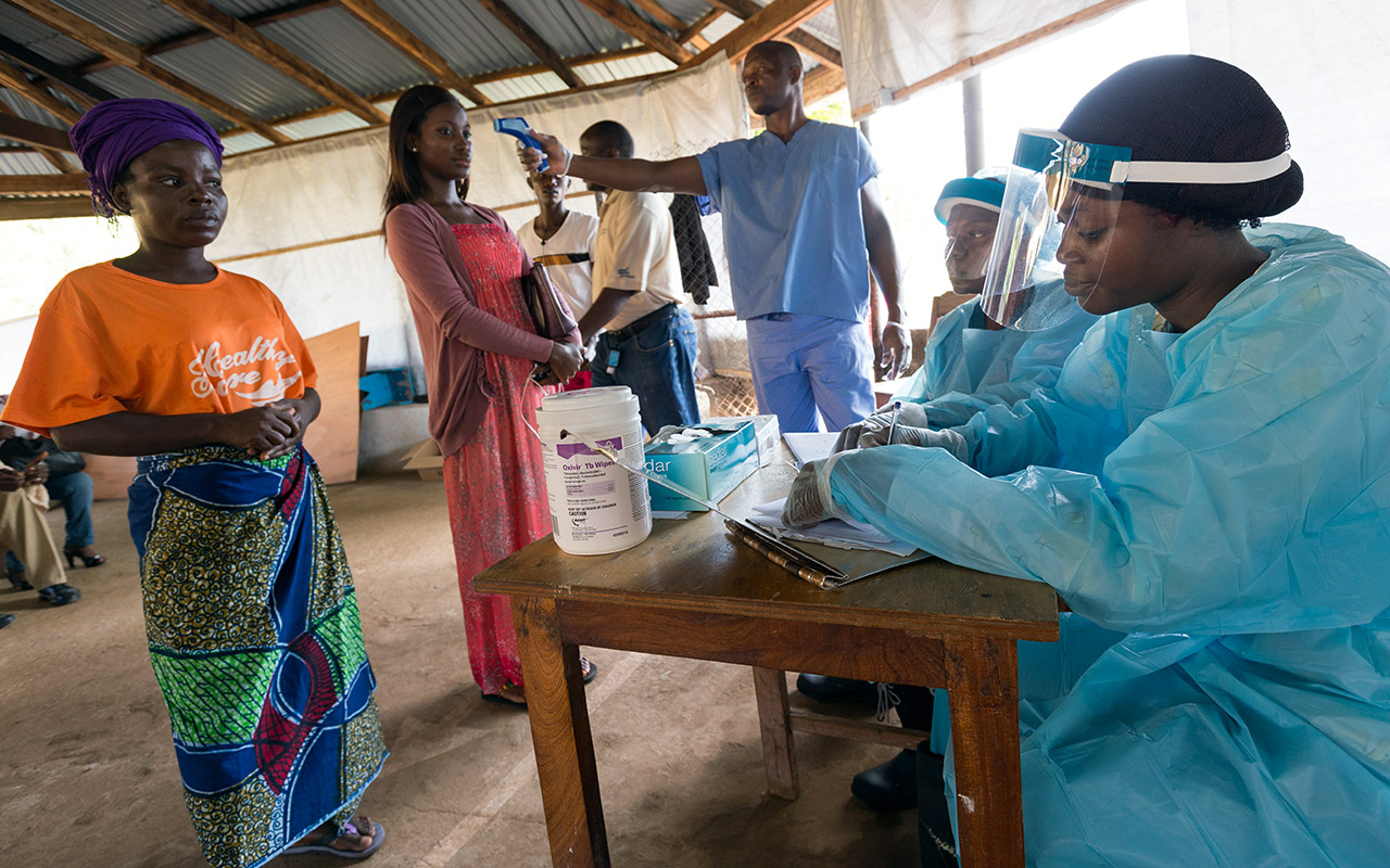 In front of a hospital in Liberia, an employee checks the temperature of the outpatients with an infrared thermometer. Photo: Christoph Püschner / Diakonie Katastrophenhilfe
