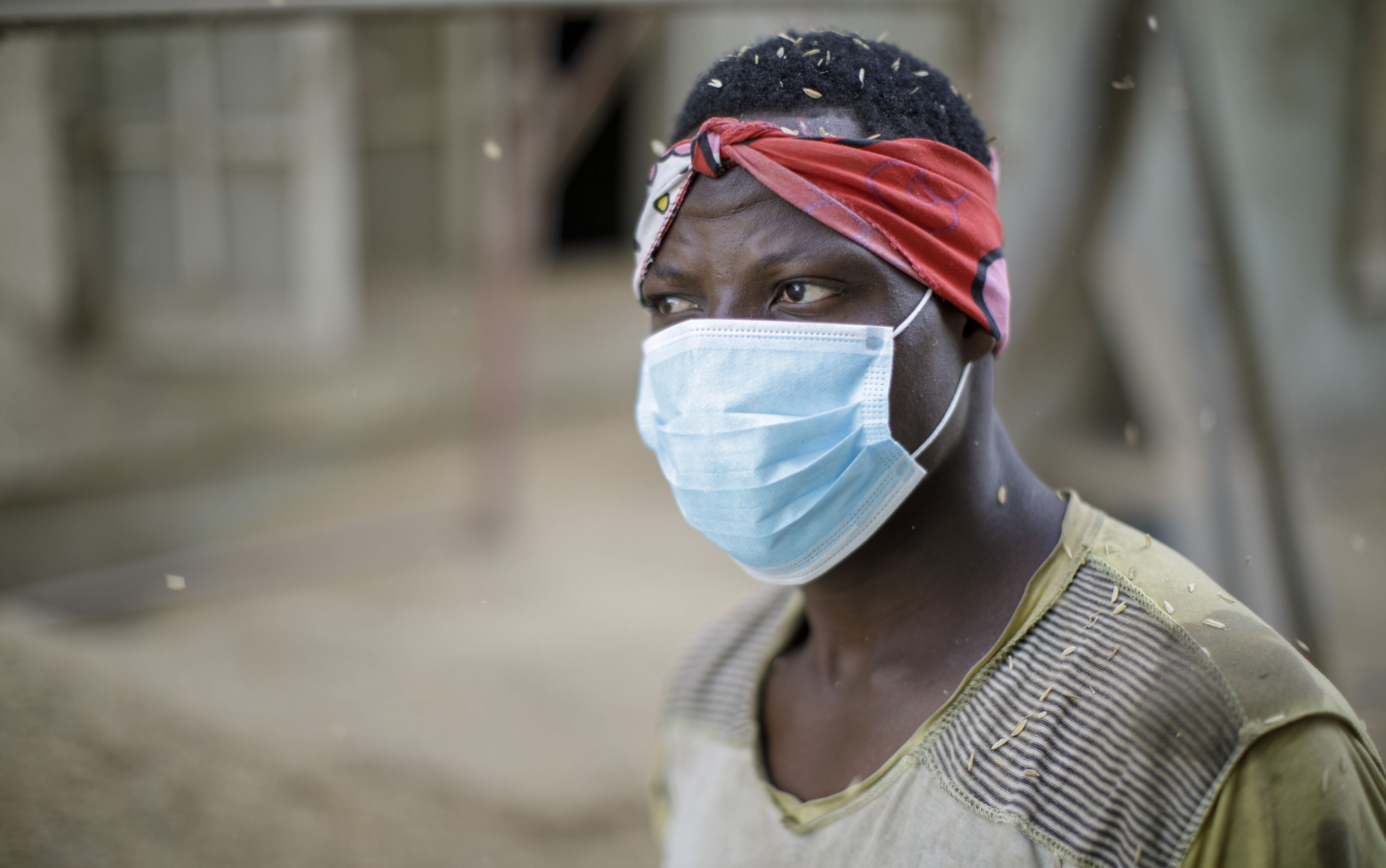 A person wearing a face mask and red headband stands in a dusty environment with particles floating around.