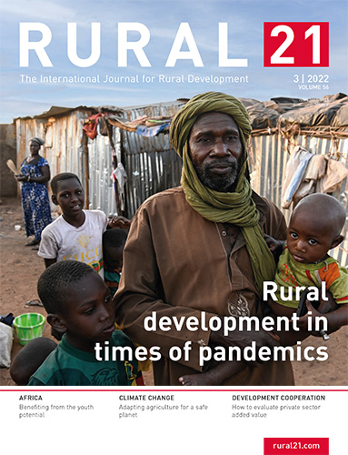 A man and children stand in front of makeshift shelters, highlighting rural development challenges during pandemics.