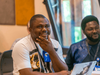 Zwei Männer in einem Büro lächeln, während einer von ihnen nachdenklich seinen Laptop betrachtet.